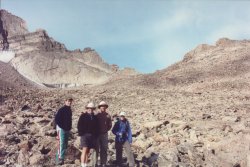 the four hikers on stony, bare ground with a mountain rising in the background