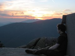 hiker reclines on an old foundation, with sun streaming brightness from behind a distant mountaintop